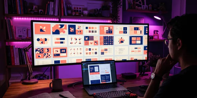 A grid of layout boards filling a wide monitor, a laptop open in front of it